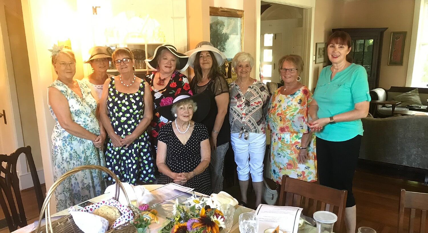 A group of nine ladies, some wearing hats, gathered for a picture at a special event in a home