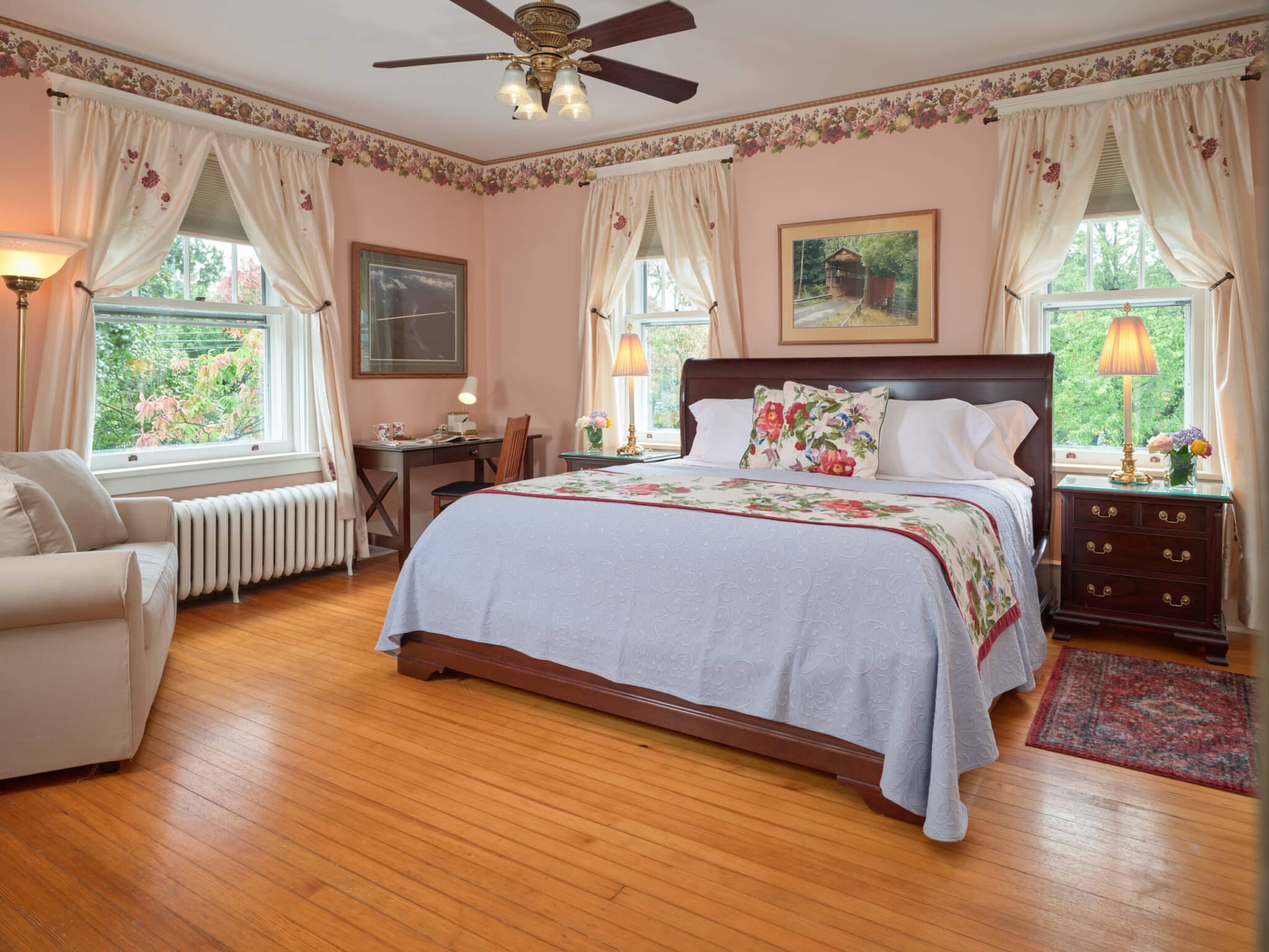 Bright guest room with queen bed in green and purple linens and two side tables with lamps