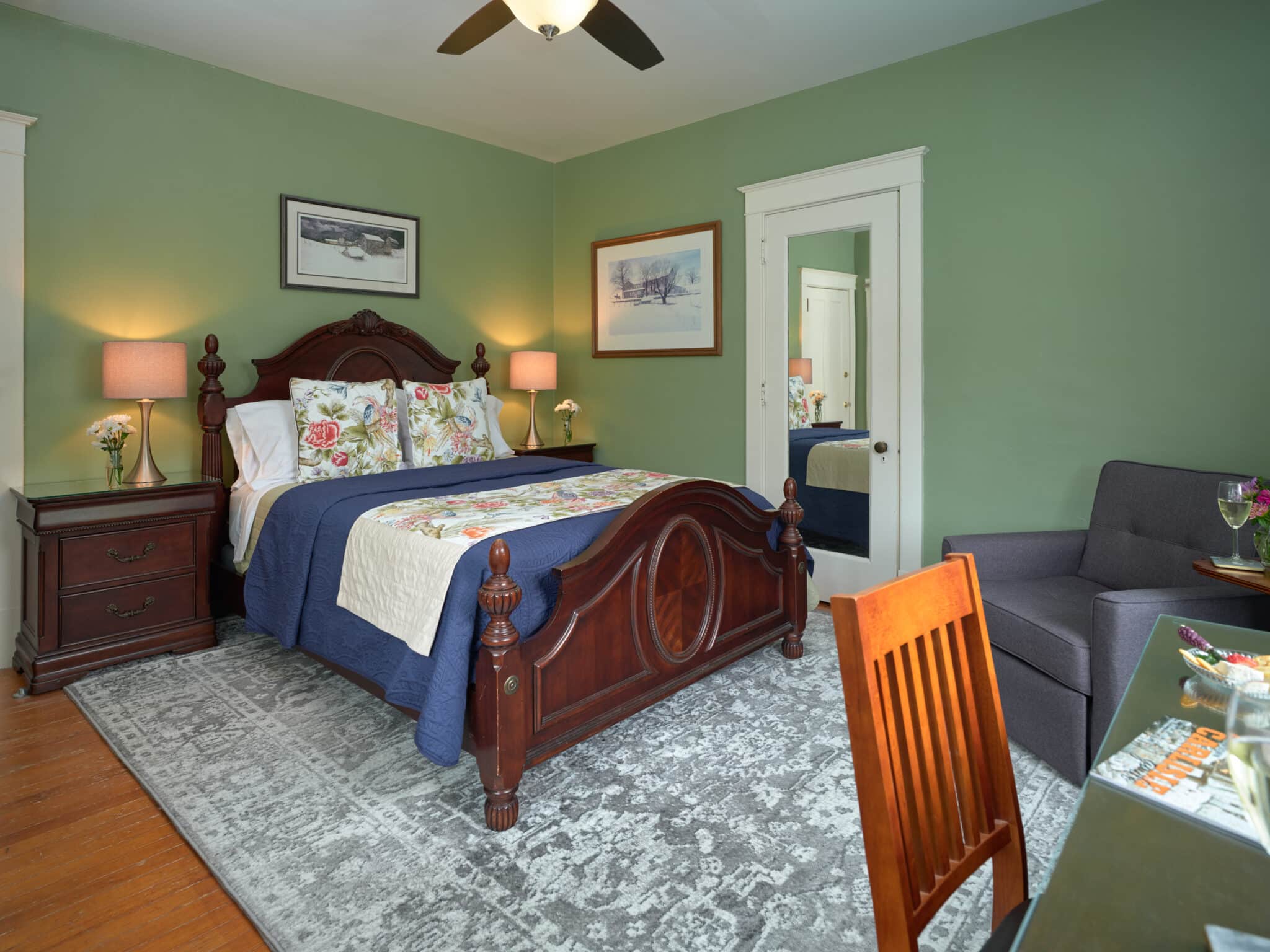 Guest room with writing desk in front of a large window, sitting chair with side table and lamp