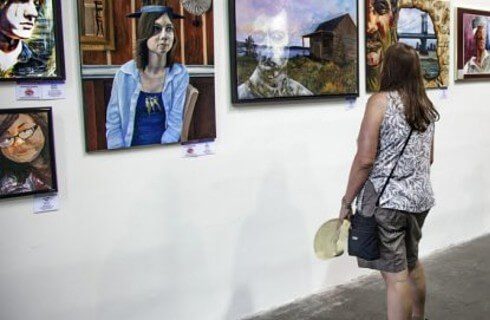 A woman in shorts and a tank top looking at a wall full of hanging artwork