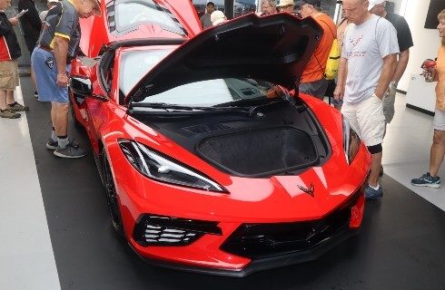 Shiny red sports car with hood and rear hatch open and people looking inside