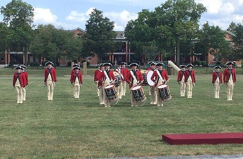 A group of people in Revolutionary War attire, holding instruments and walking across a lawn