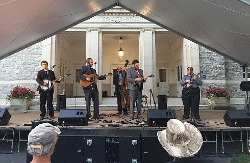 A group of five men placing various instruments on an outdoor stage under a large awning