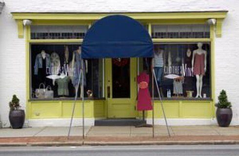 Outside view of a storefront with a blue awning, green trim and clothing displays in the windows