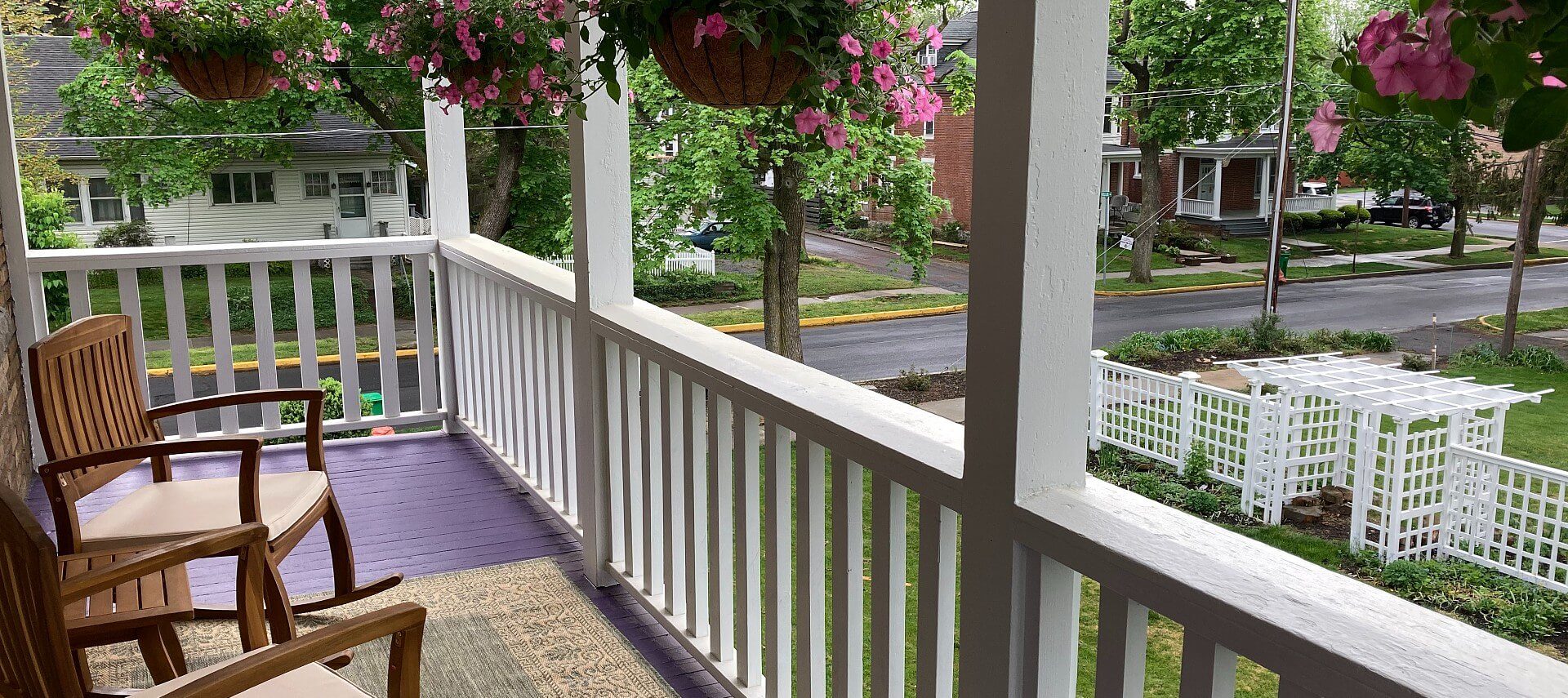 Upper balcony of a home with white railing, hanging flowers and sitting chairs with side table