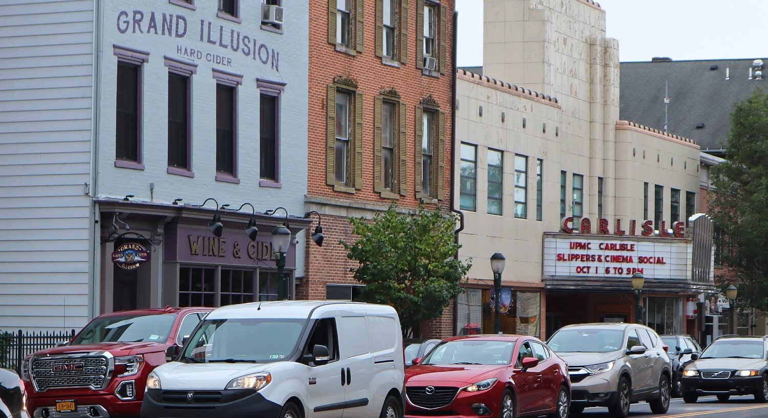 A downtown main street with two lanes of cars lined up next to the storefronts