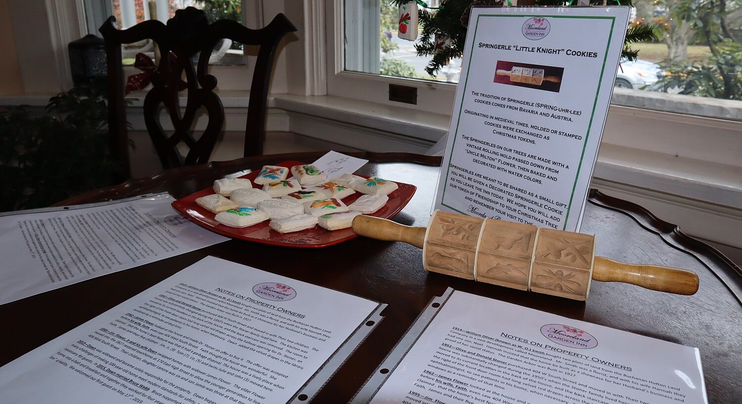 Round table with plate of cookies, decorative rolling pin and several printed papers with text