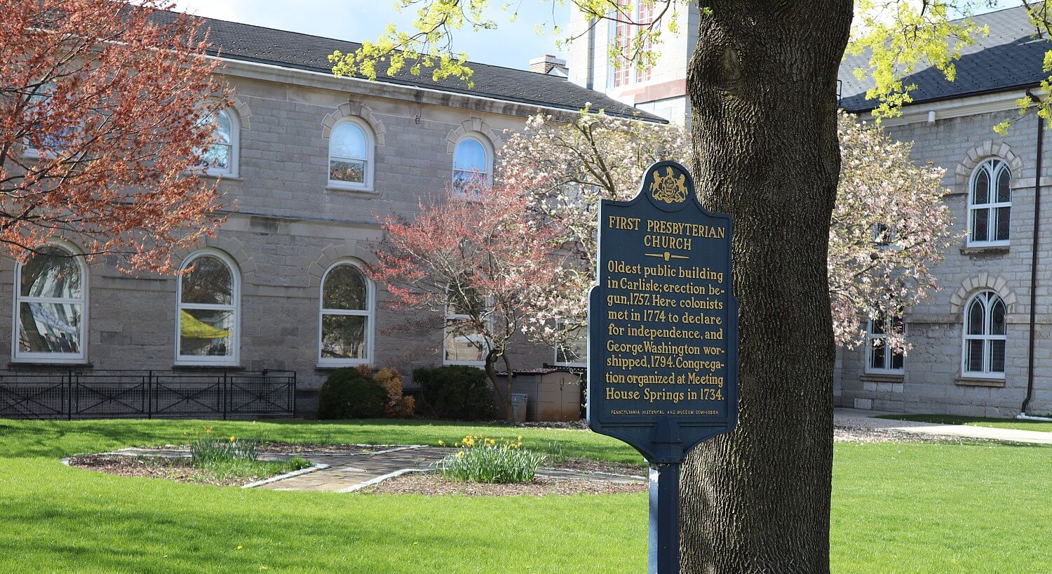 Outside of a historic church with numerous arched windows and green lawn with trees