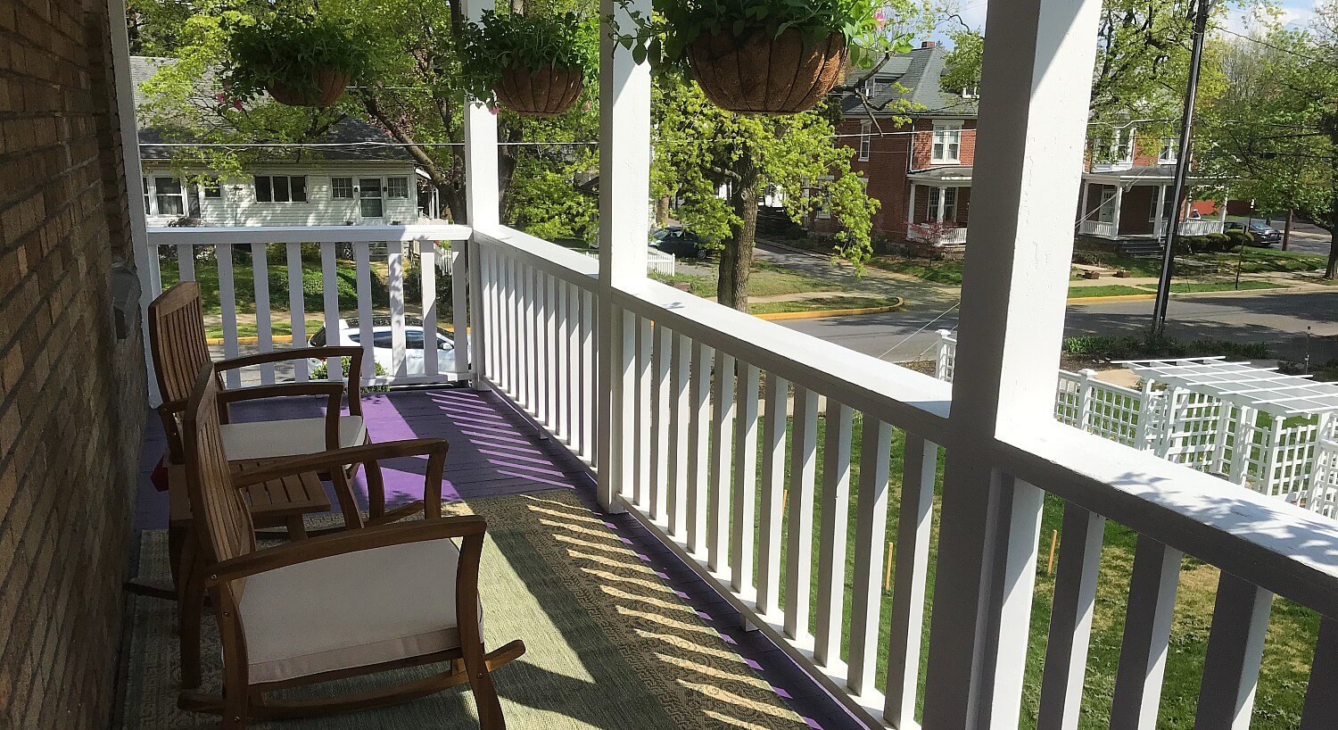 Upper balcony porch of a home with white railing, hanging flowers and two sitting chairs with side table