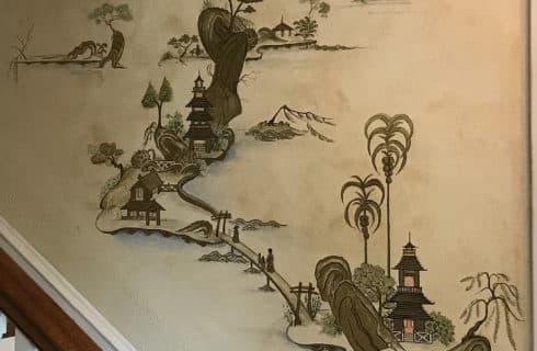 Decorative Japanese drawings going up the wall by a staircase with a brown banister
