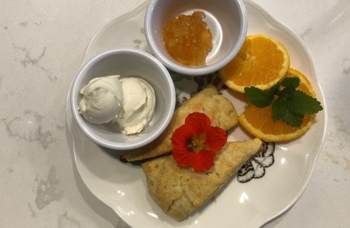 White plate with two scones and two small dishes with whipped cream and orange marmalade