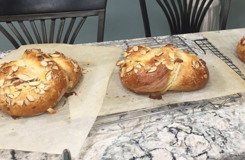 Golden brown loaves of bread with sliced almonds cooling on wire racks on a marbled countertop