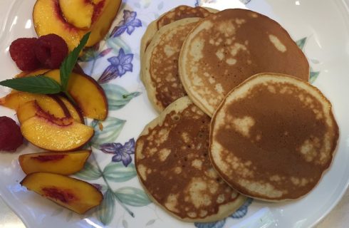 Flowered plate with five golden pancakes, sliced nectarines and raspberries