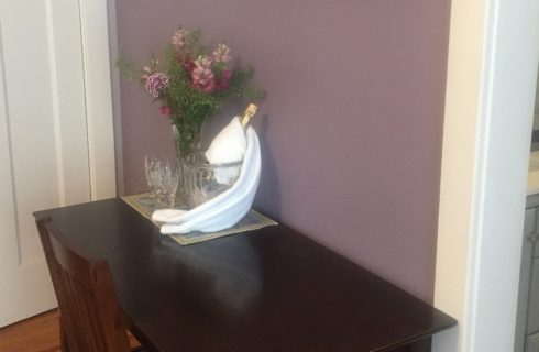 Dark brown desk with a vase of flowers and champagne bottle with a glass against a purple wall