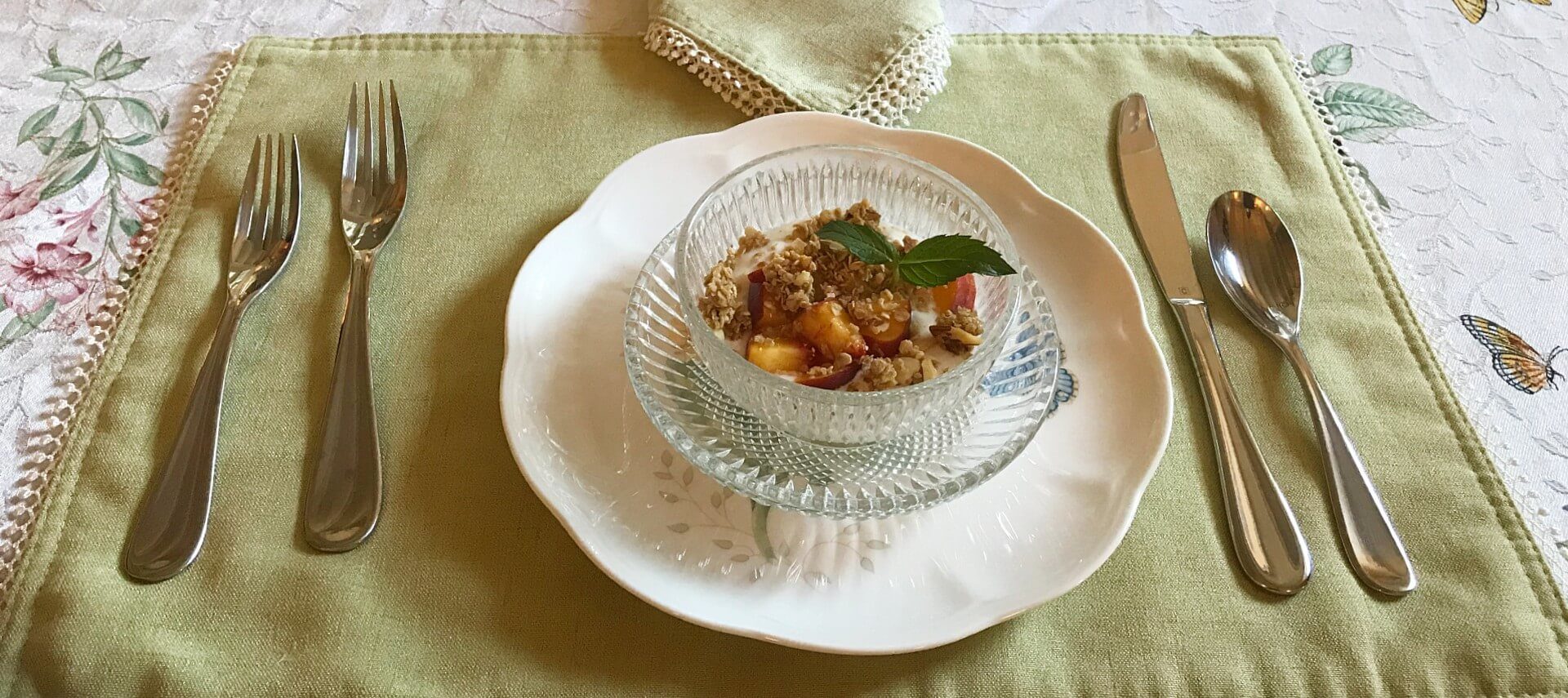 Place setting set for breakfast with glass dish of yogurt, fruit and granola