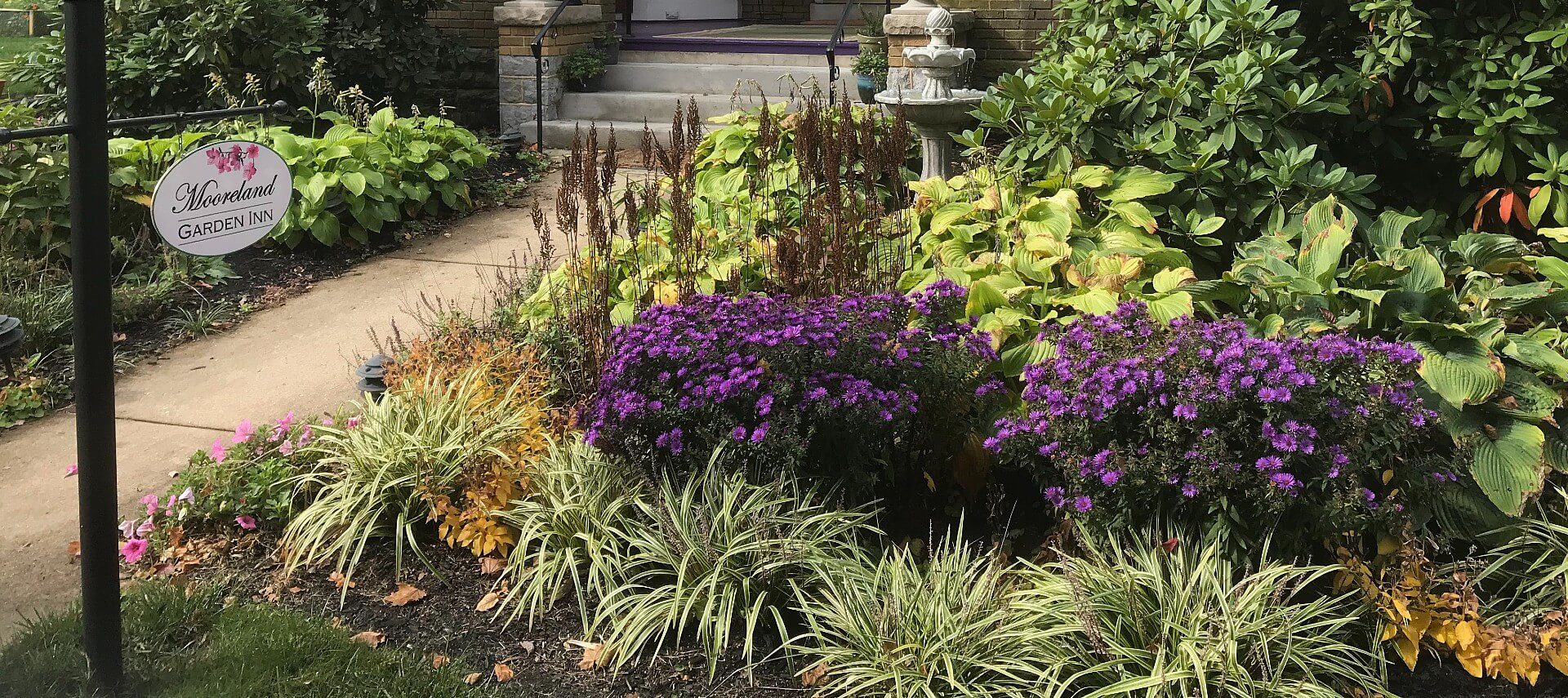 Sign post near a lush and colorful garden bed by the front steps of a home