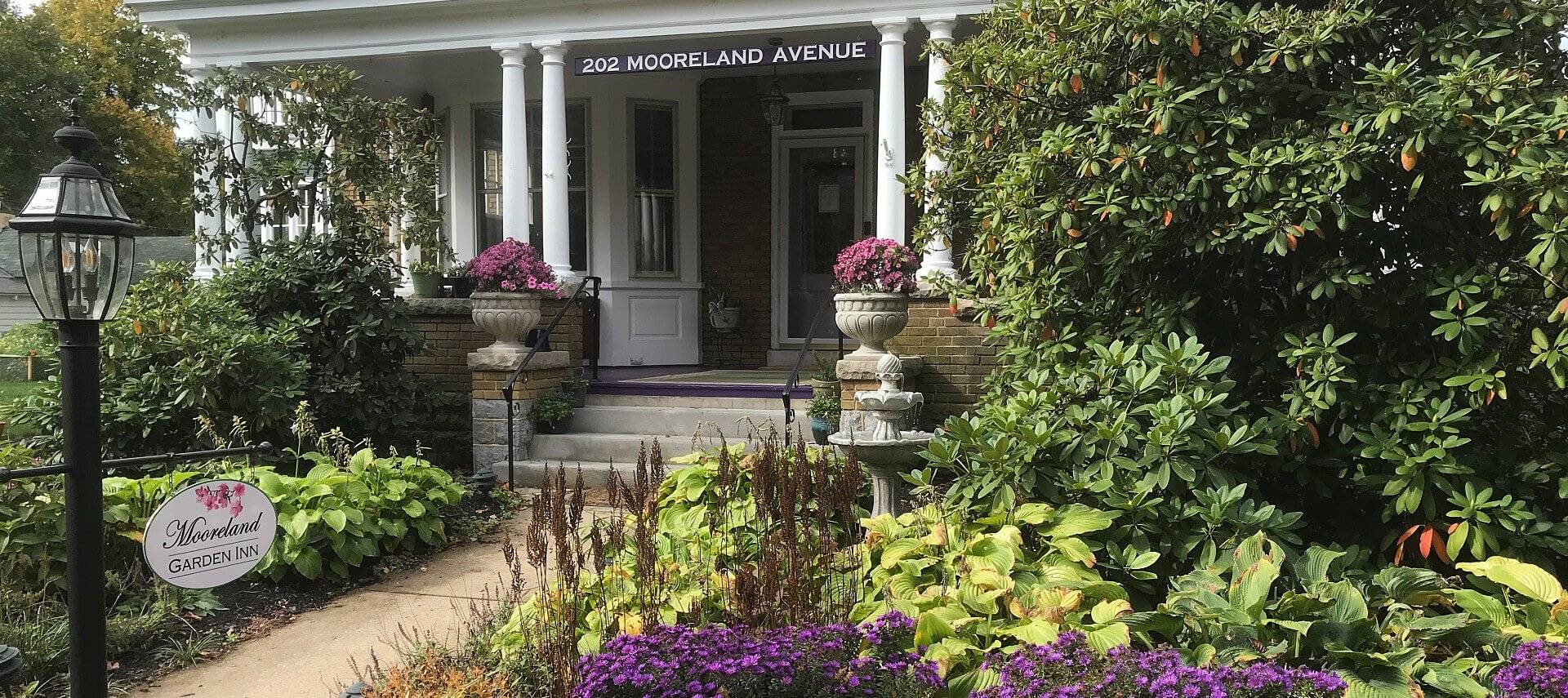 Front facade of a bed and breakfast showing a porch with white columns and abundant landscaping